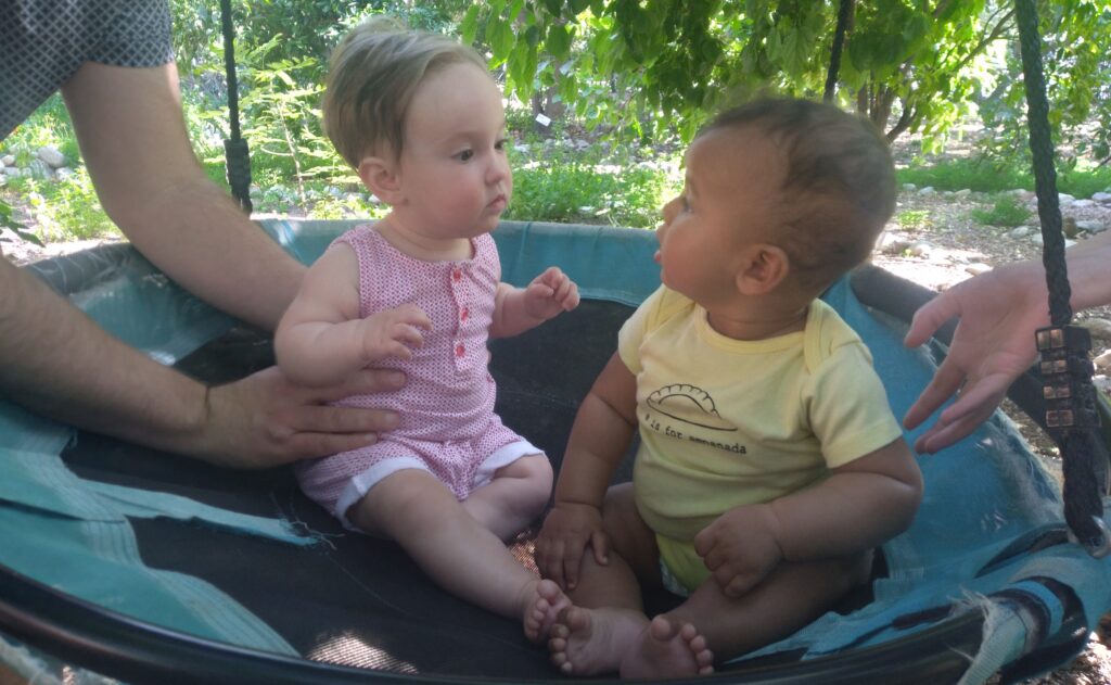 Two birth doula client's babies sit supported together on a swing